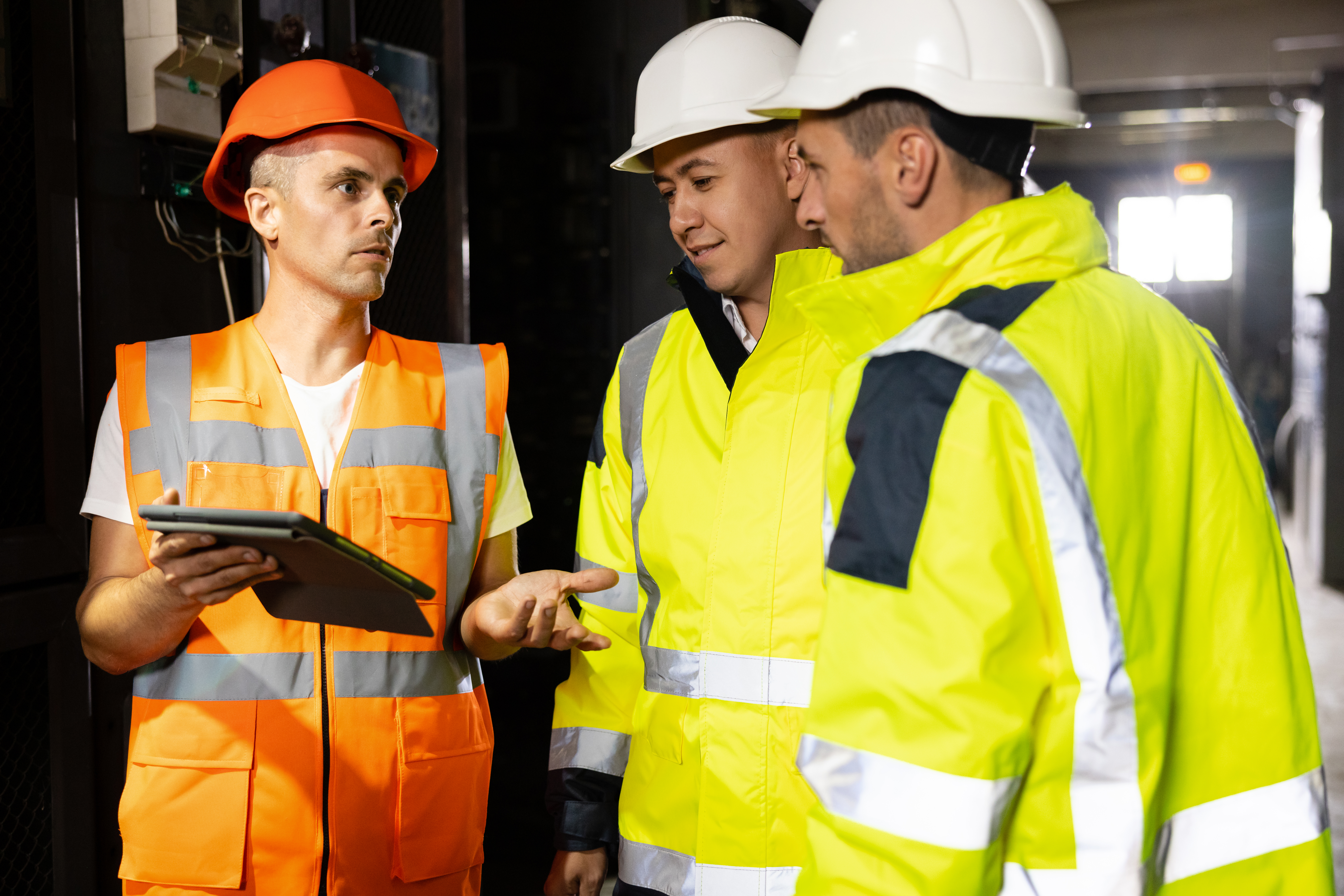 Three Heavy Industry Engineers and Worker Stand in Pipe Manufacturing Factory, Use Digital Tablet Computer, Have Discussion. Design and Construction of Oil, Gas and Fuels Transport Pipeline.